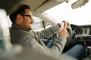 Young white male with glasses looking at cellphone while driving