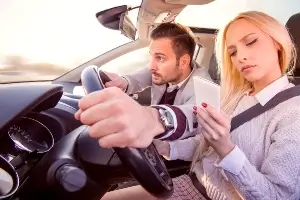 blonde teen driver texting while male passenger takes wheel
