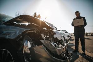 man with laptop by damaged car