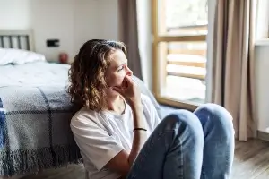 young woman sitting on the floor looking upset and traumatized, gazes out of window